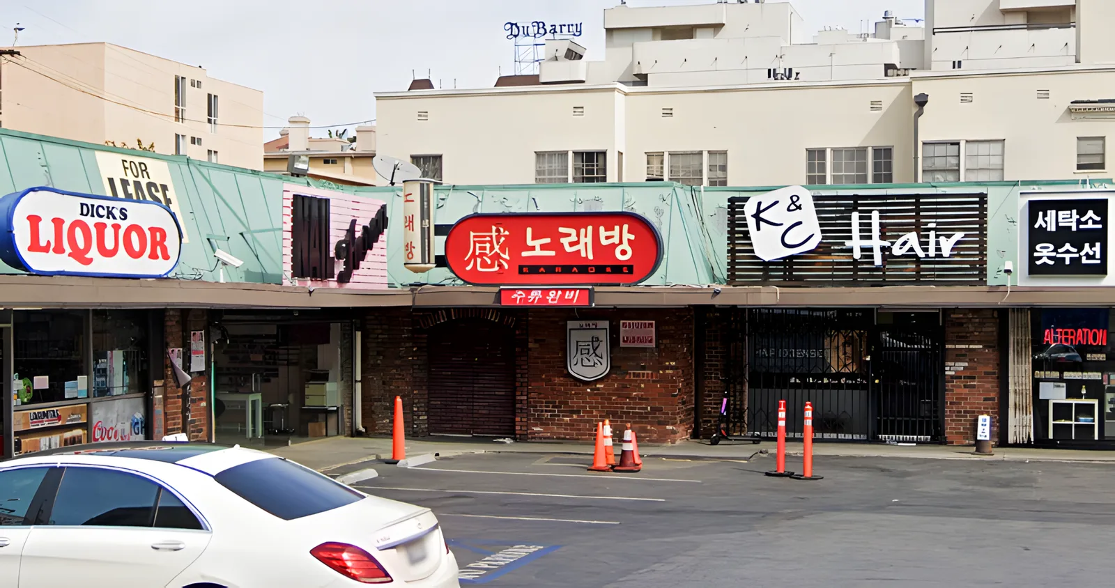 Strip mall storefronts with Korean signage and parked cars