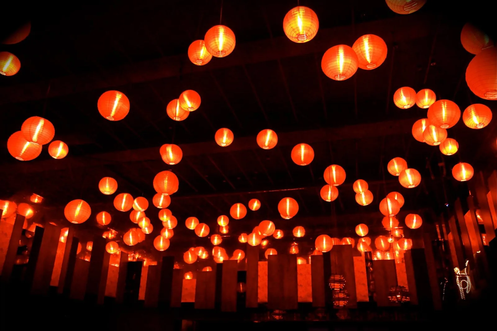 Dark bar ceiling densely hung with glowing red paper lanterns