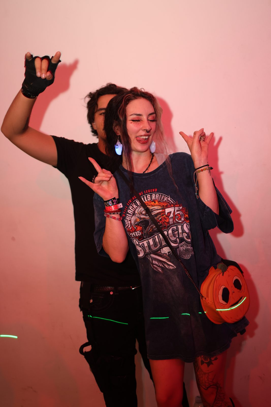 Two guests throw hand signs, one in a graphic tee with a pumpkin bag
