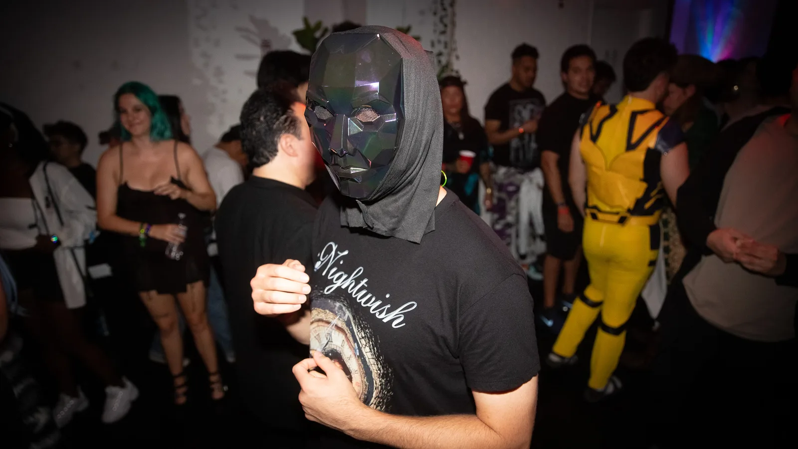A guest in a mesh mask hugs another guest amid the crowd
