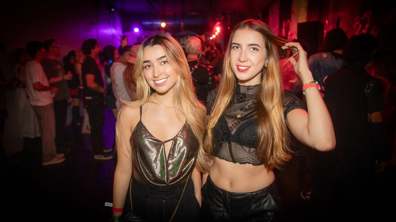 Two guests pose together in black going-out looks under club lighting