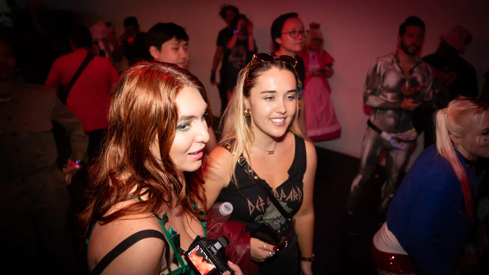 Two guests lean together, one holding a small camera