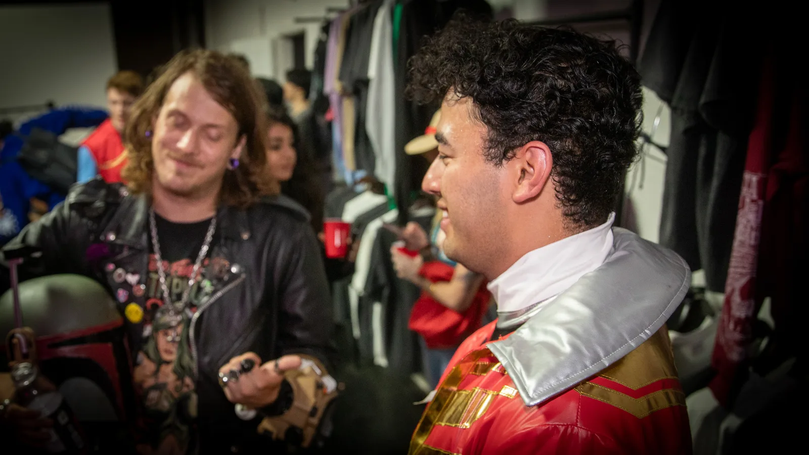 Two guests in costume talk near a rack of jackets