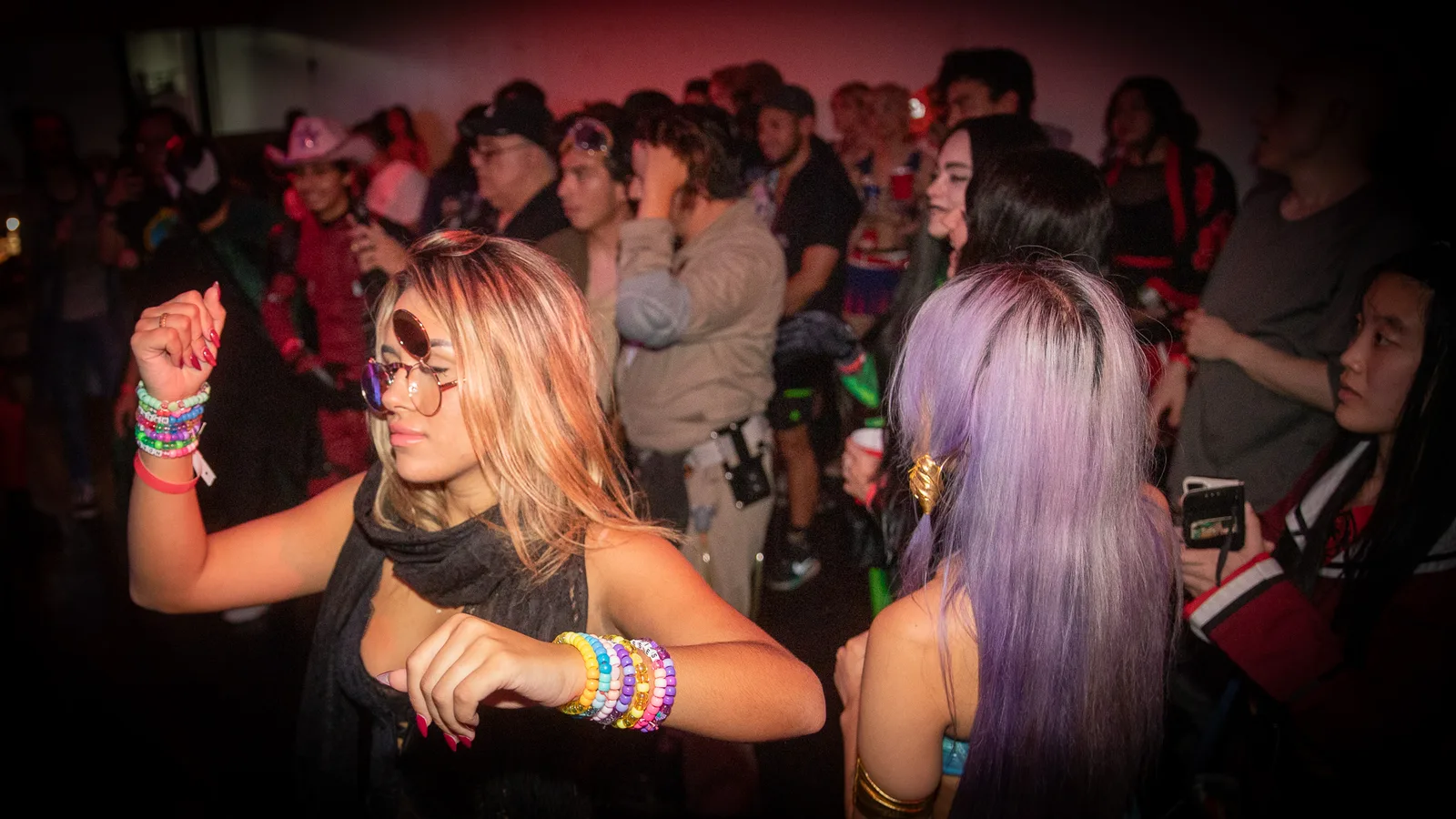 A guest with beaded bracelets dances beside a guest in a lilac wig