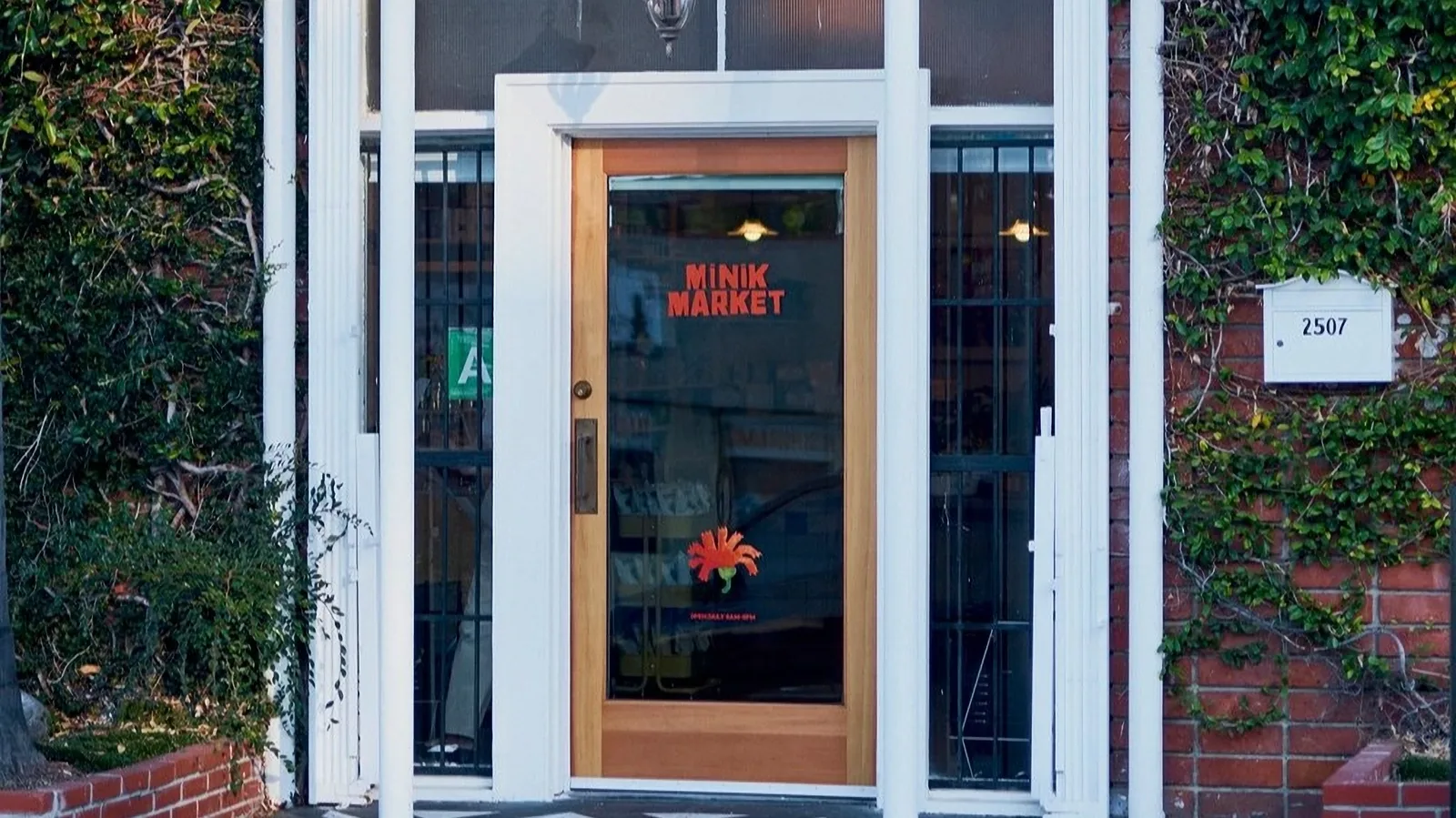Minik Market front door with glass door, brick walls, white frame, and plants