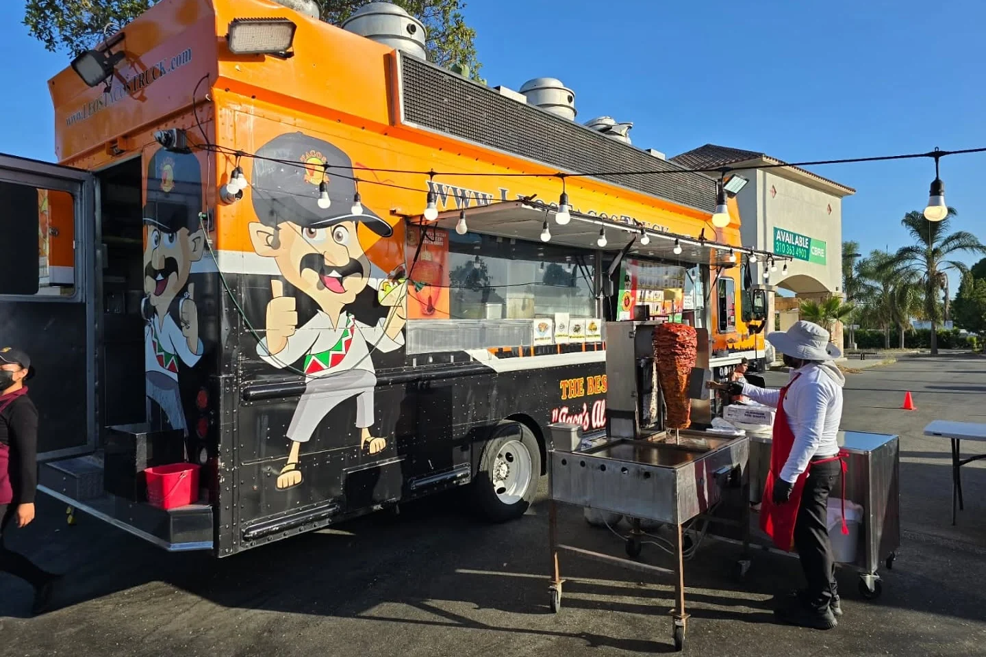 A taco truck parked at the curb with the griddle going