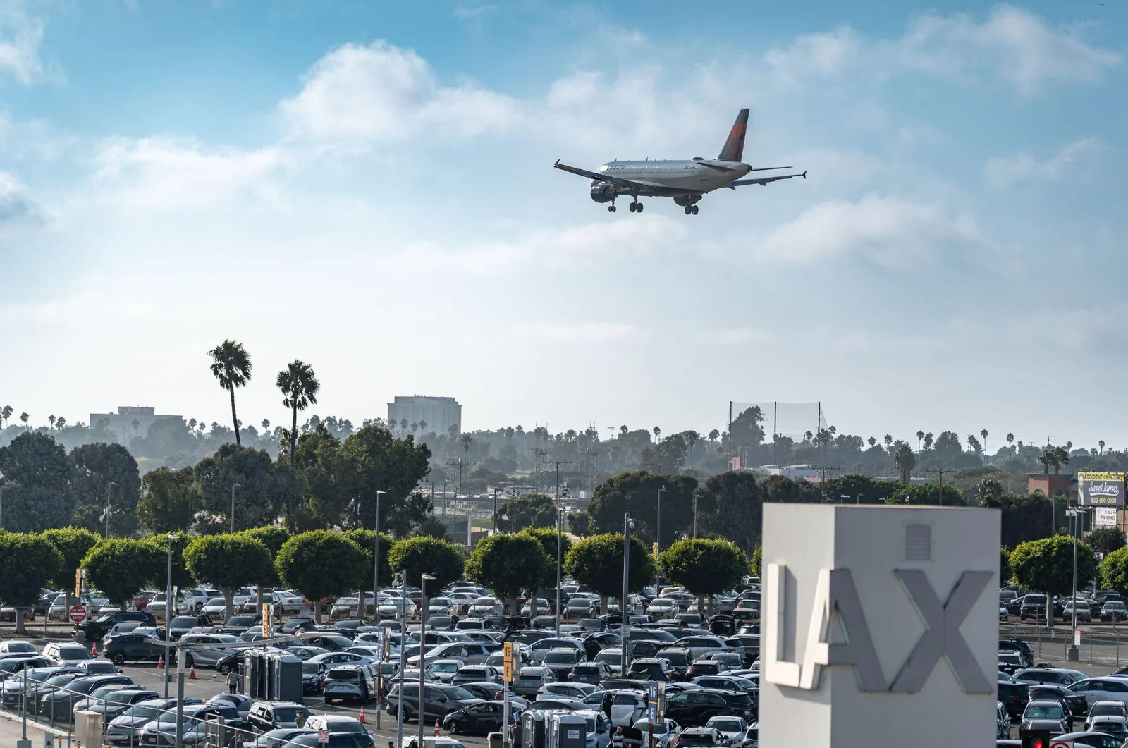 An aircraft on final approach to LAX passing above rows of parked cars