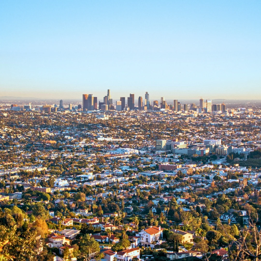 Wide aerial shot of Los Angeles homes and buildings with the city skyline in the distance on a sunny day