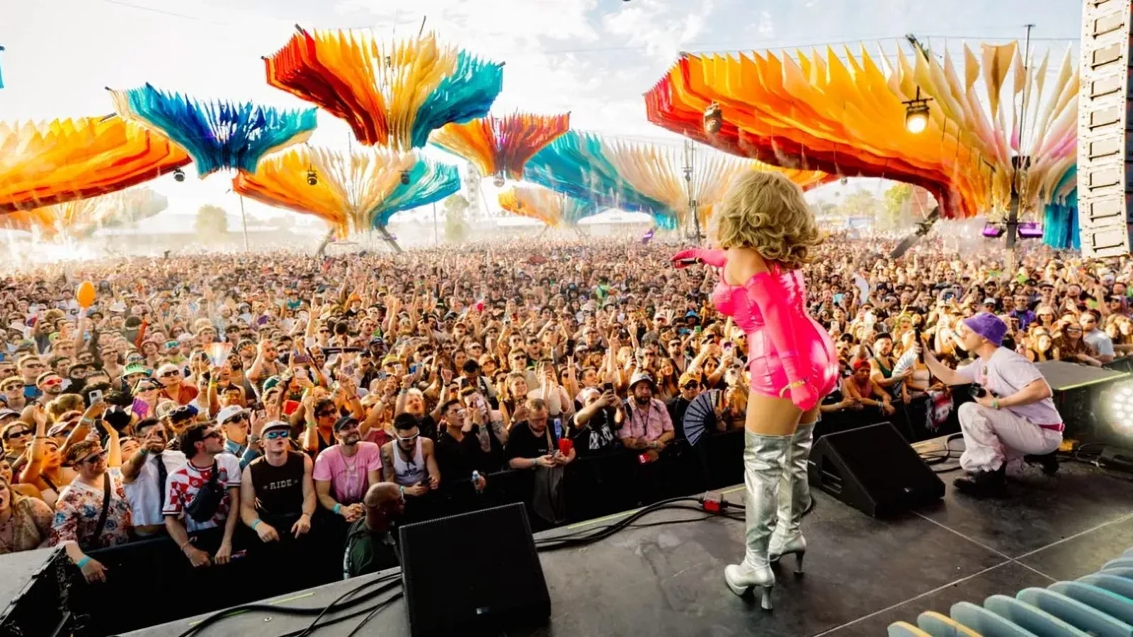 Performer in pink faces a huge festival crowd under colourful hanging sculptures