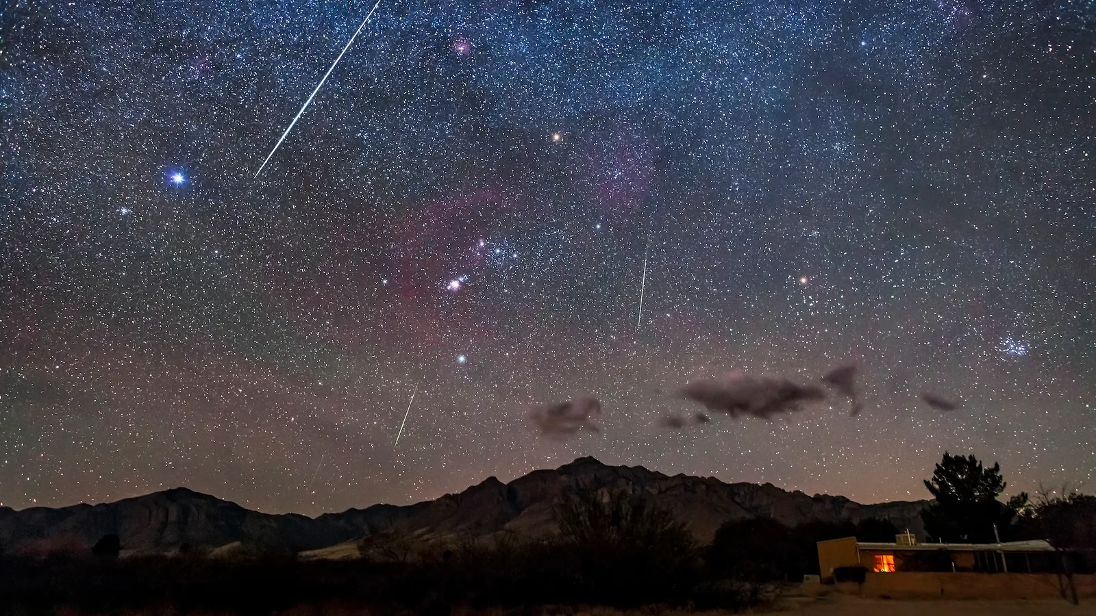 Meteor streaking across a star filled night sky above a dark mountain ridge