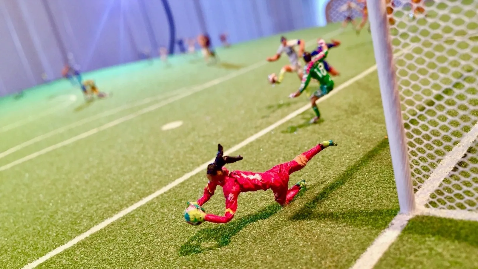 Goalkeeper in red dives for the ball as attackers close in