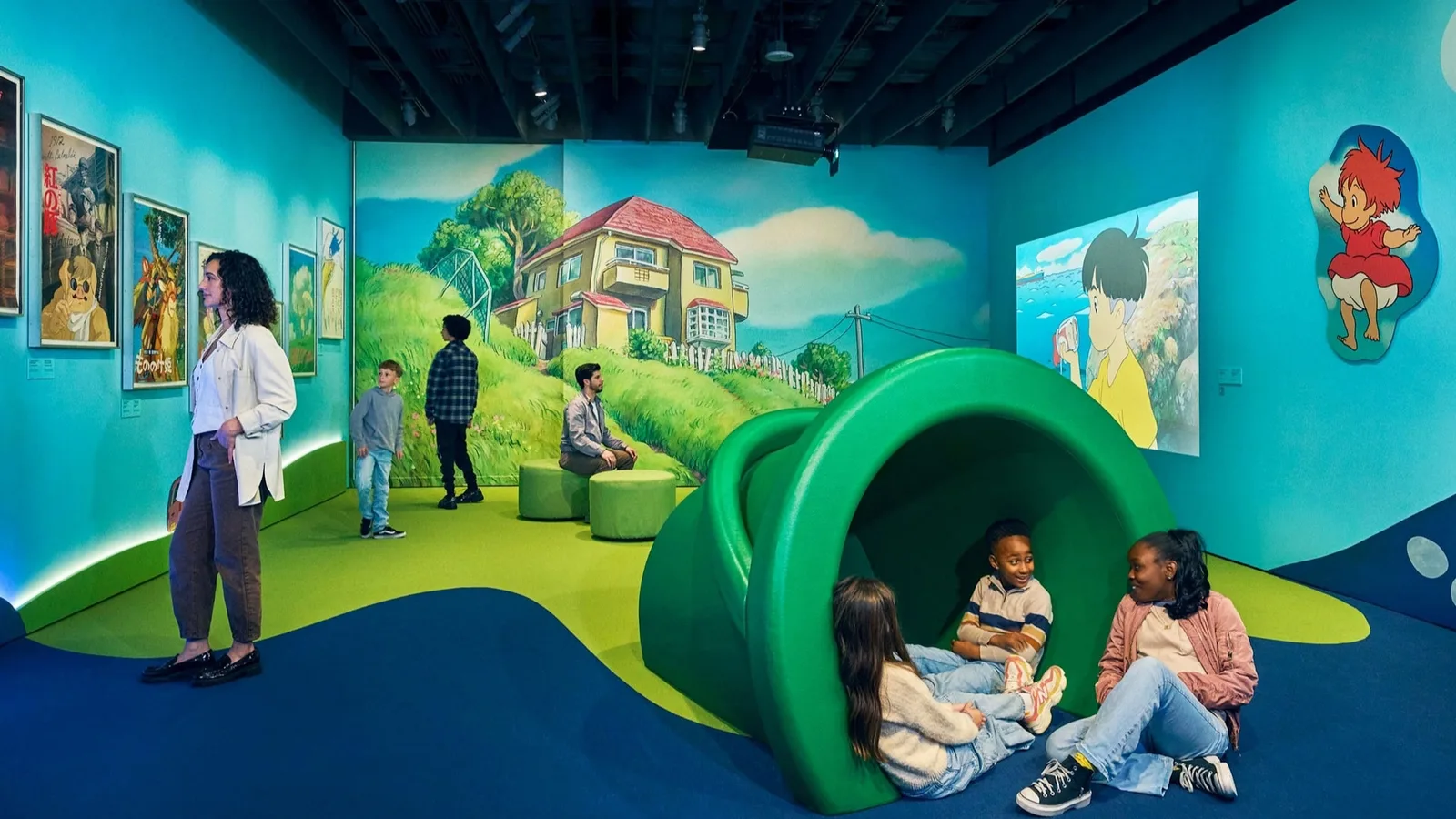 Children sit inside a green tunnel in a painted museum play space