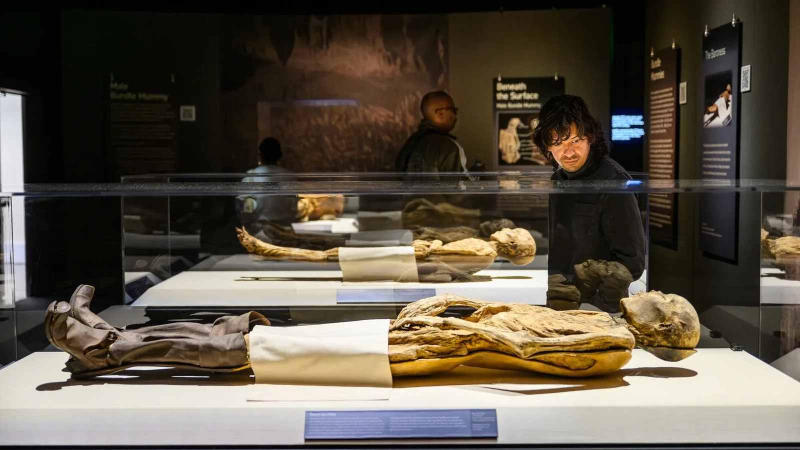 Visitors view mummified remains laid out in lit museum display cases
