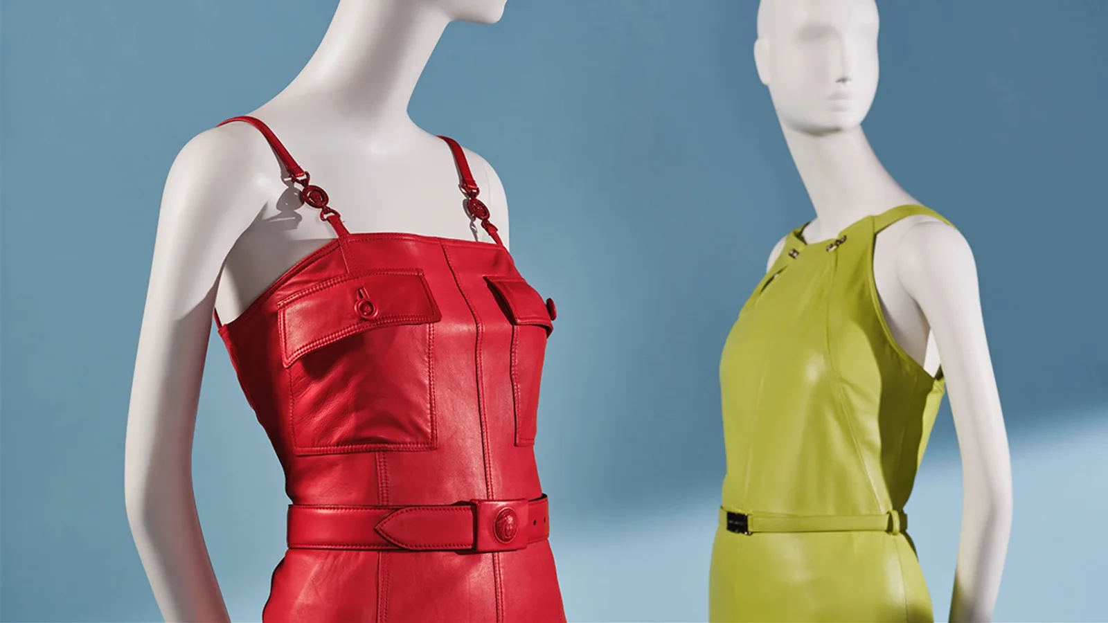 Two mannequins in red and lime green leather outfits on a blue background