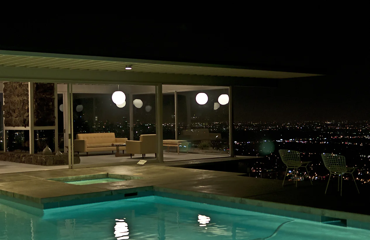 Modern glass house at night with a lit pool and city lights