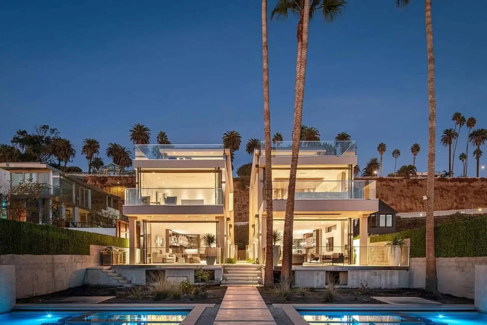 Modern white beachfront homes at dusk with palms and a pool