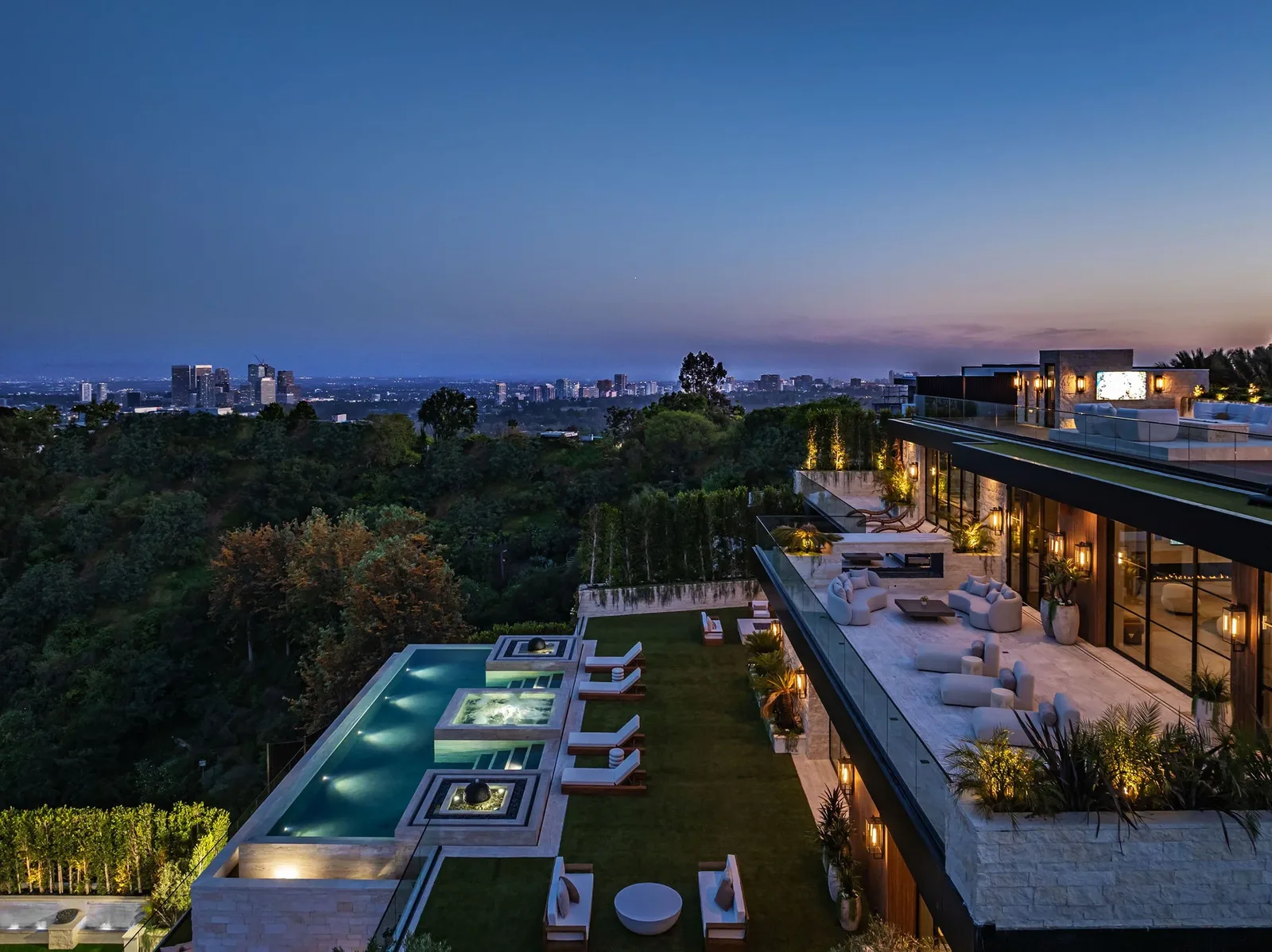 Aerial dusk view of a terraced rooftop pool above treetops