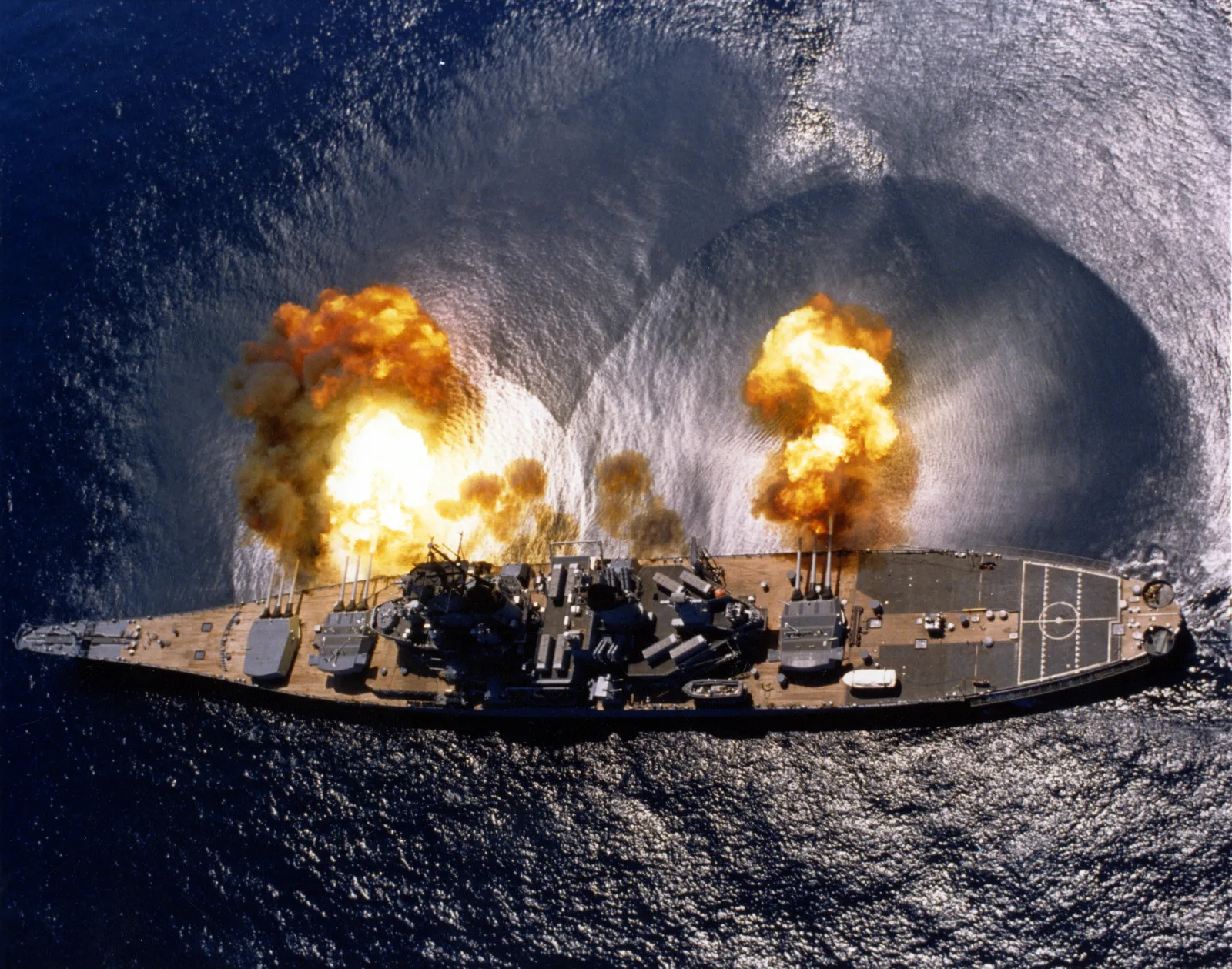 The battleship USS Iowa firing a full broadside, all guns blazing across the water.