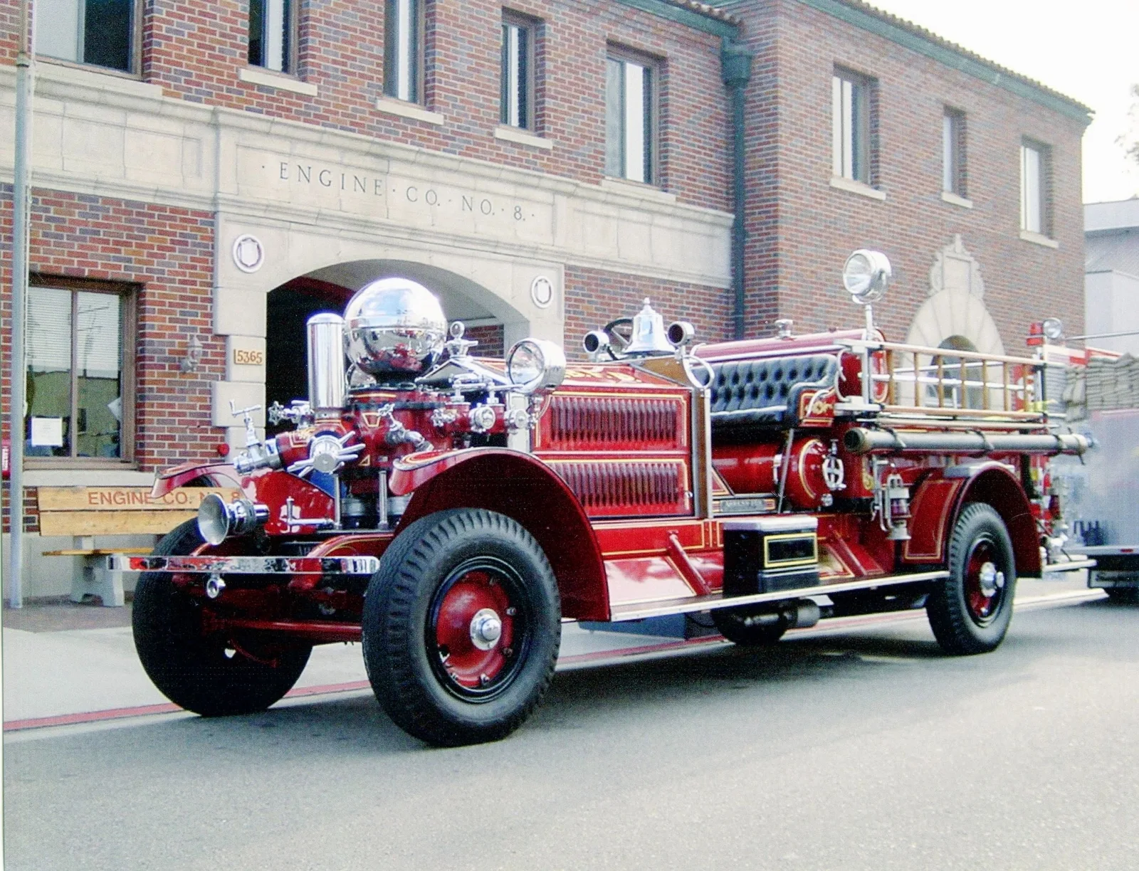 Vintage red fire engine parked outside a brick firehouse with arched doorways