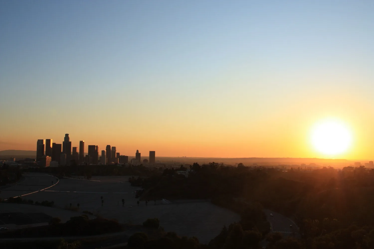 Sunset over a hazy distant skyline seen across the hills