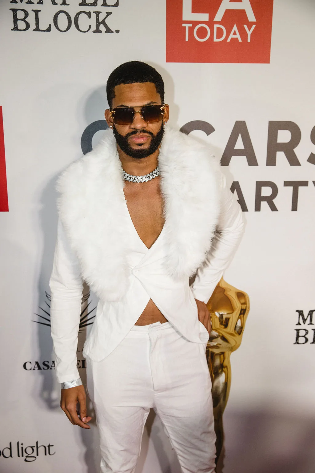 A guest in a white suit with a fur collar and chain necklace