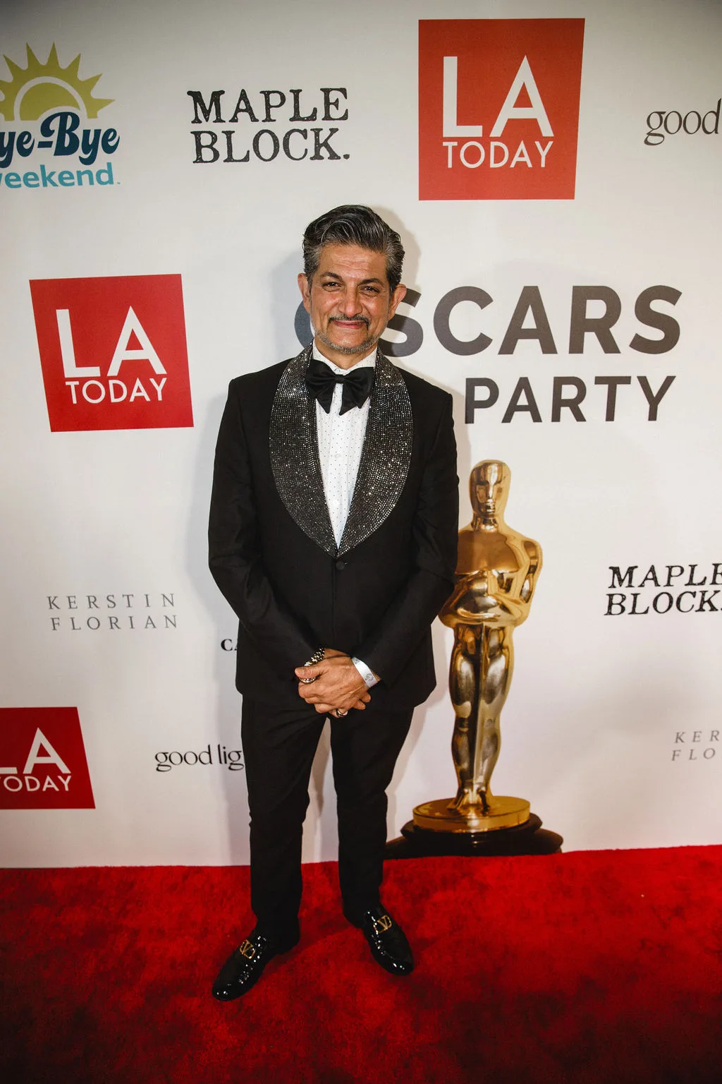 A guest in a tuxedo with a sequined lapel stands by the statuette