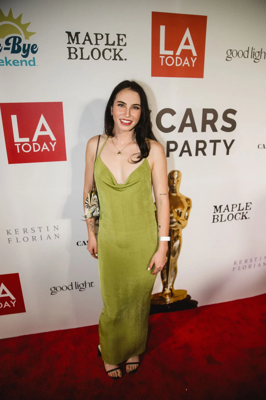 A guest in an olive green slip dress poses at the backdrop