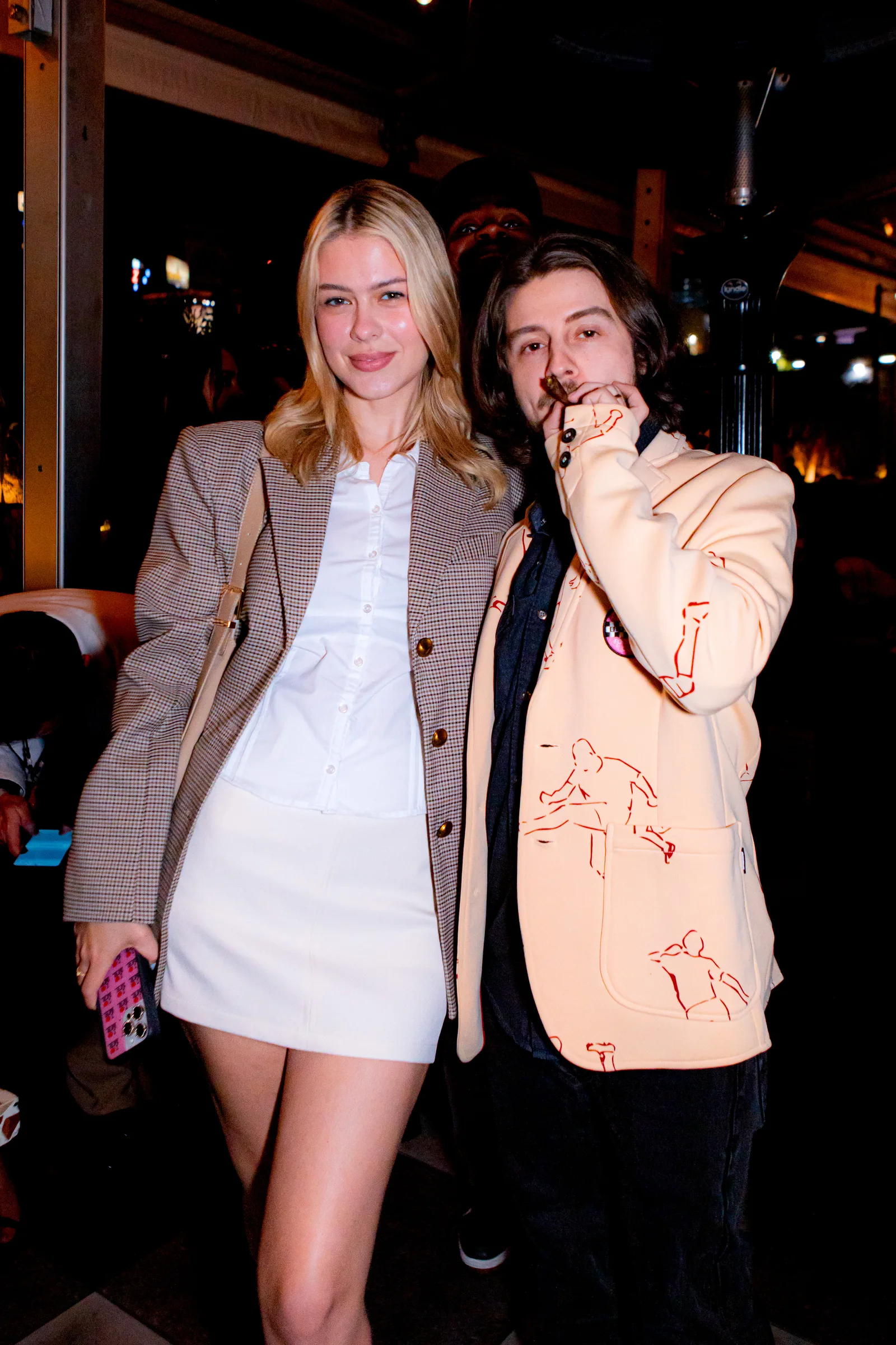 Two guests in oversized blazers pose together outdoors at night