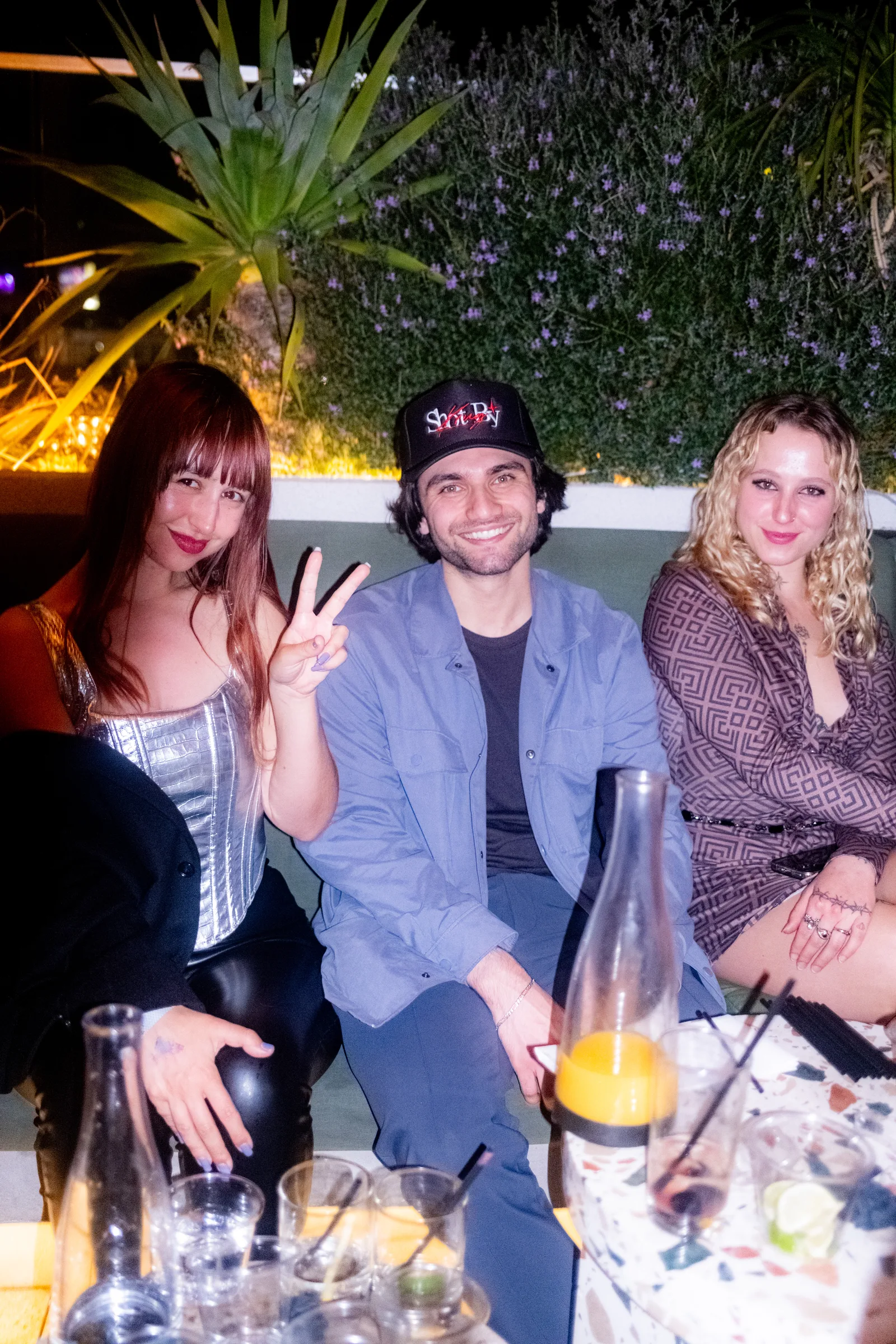 Three guests sit on a patio banquette, one flashing a peace sign