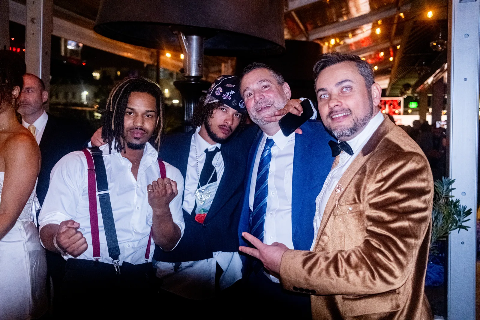 Four guests in suits and suspenders clown for the camera at night