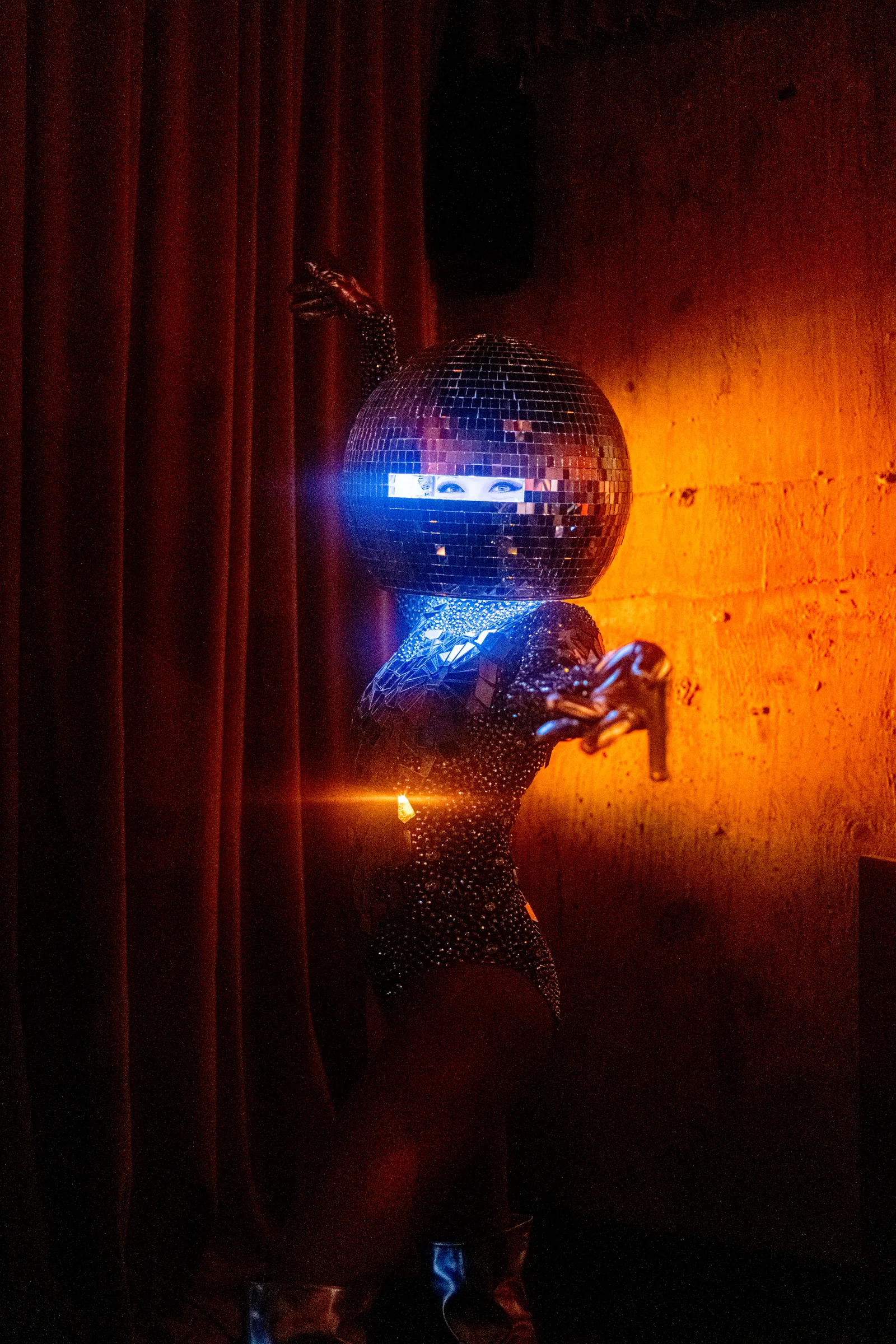 A performer in a mirrored bodysuit and disco ball helmet on stage