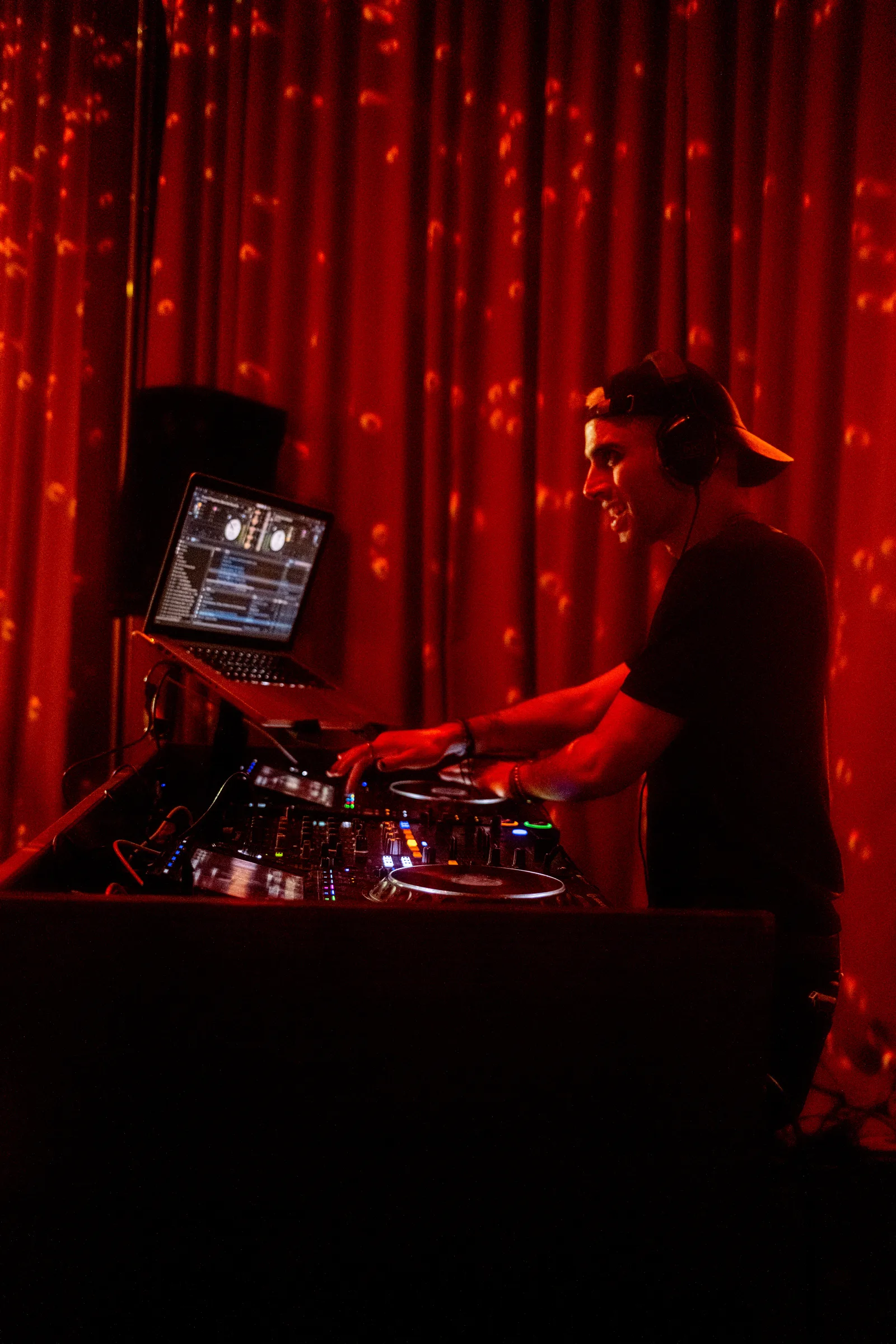 A DJ works the decks in front of a red curtain