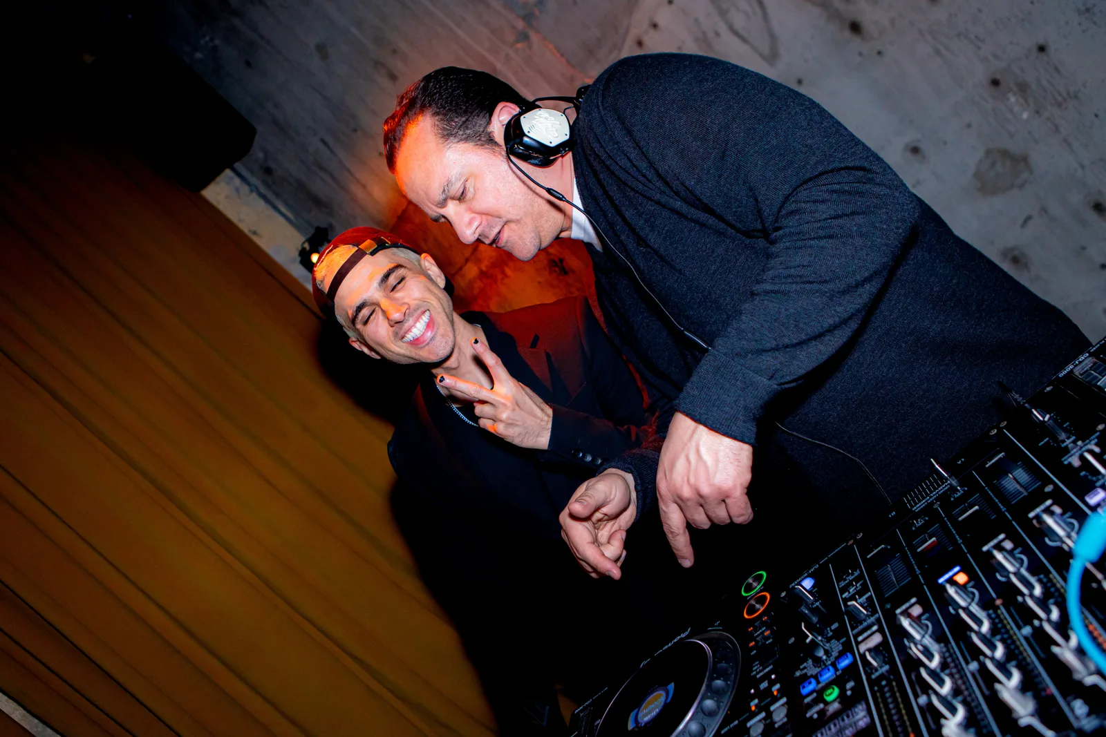 Two DJs share the booth, one leaning over the mixer