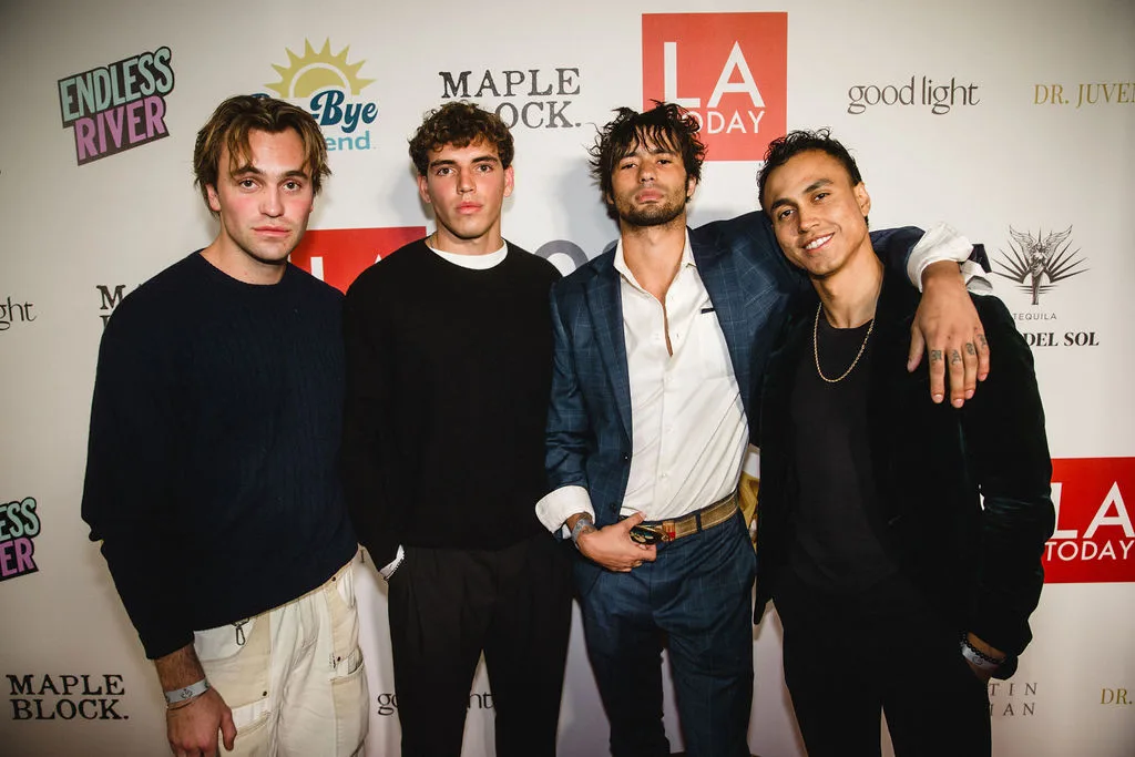 Four guests in casual dark outfits pose together on the carpet