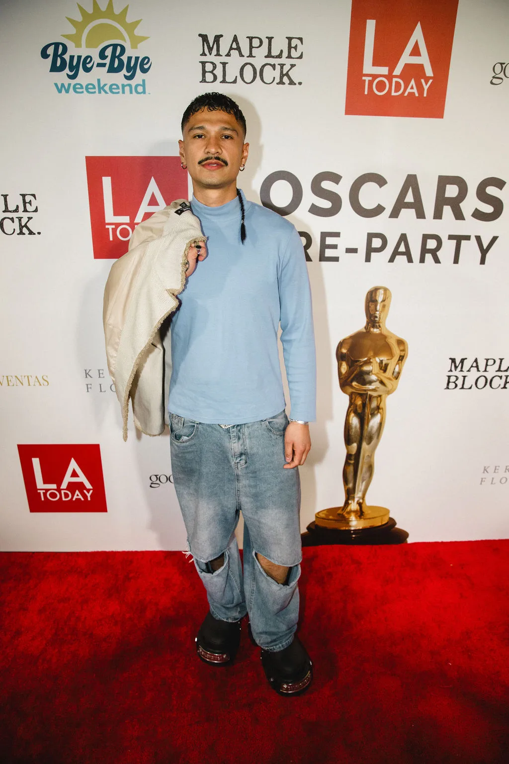A guest in a pale blue sweater and jeans poses beside a gold statuette