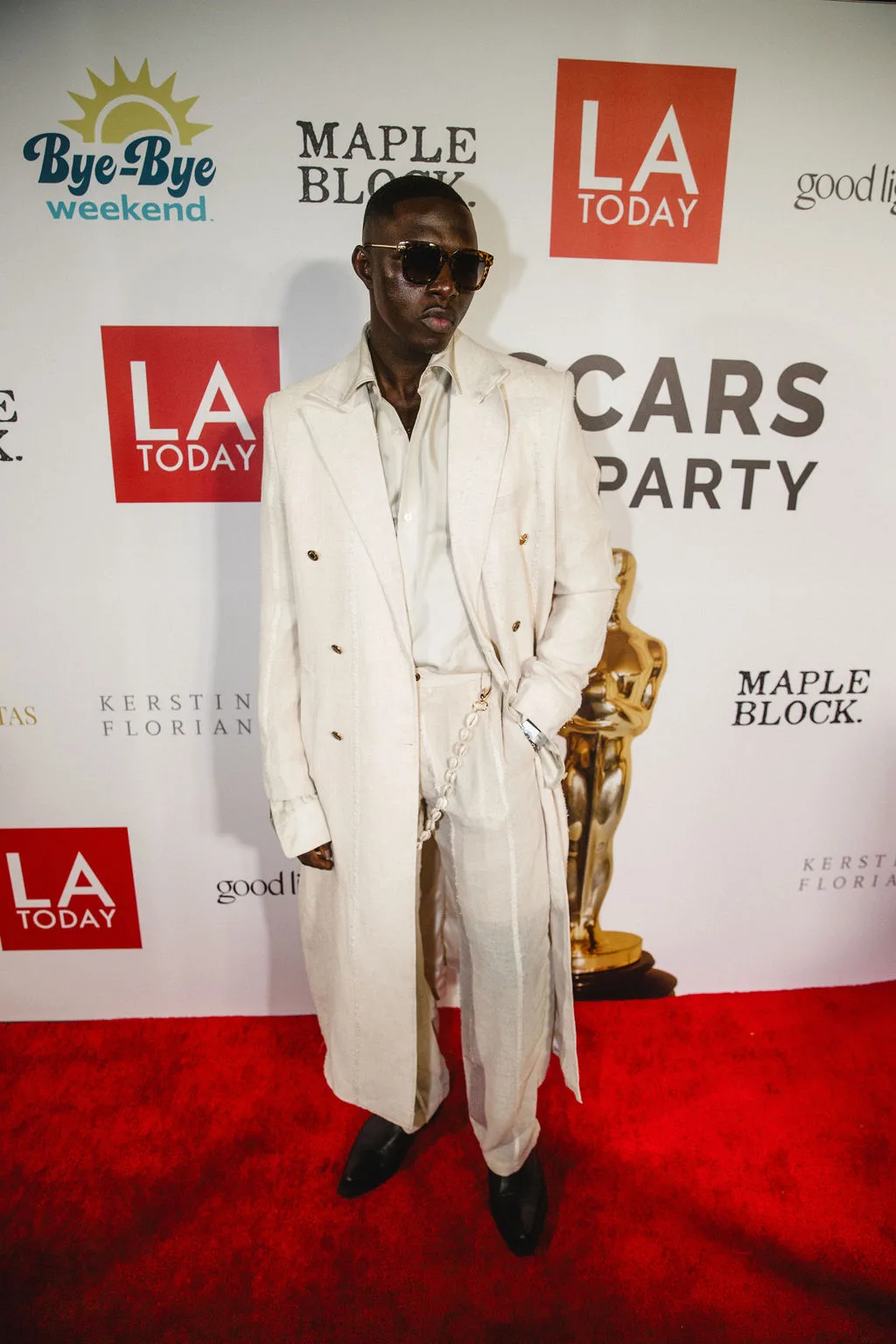 A guest in an oversized cream suit stands at the sponsor step-and-repeat