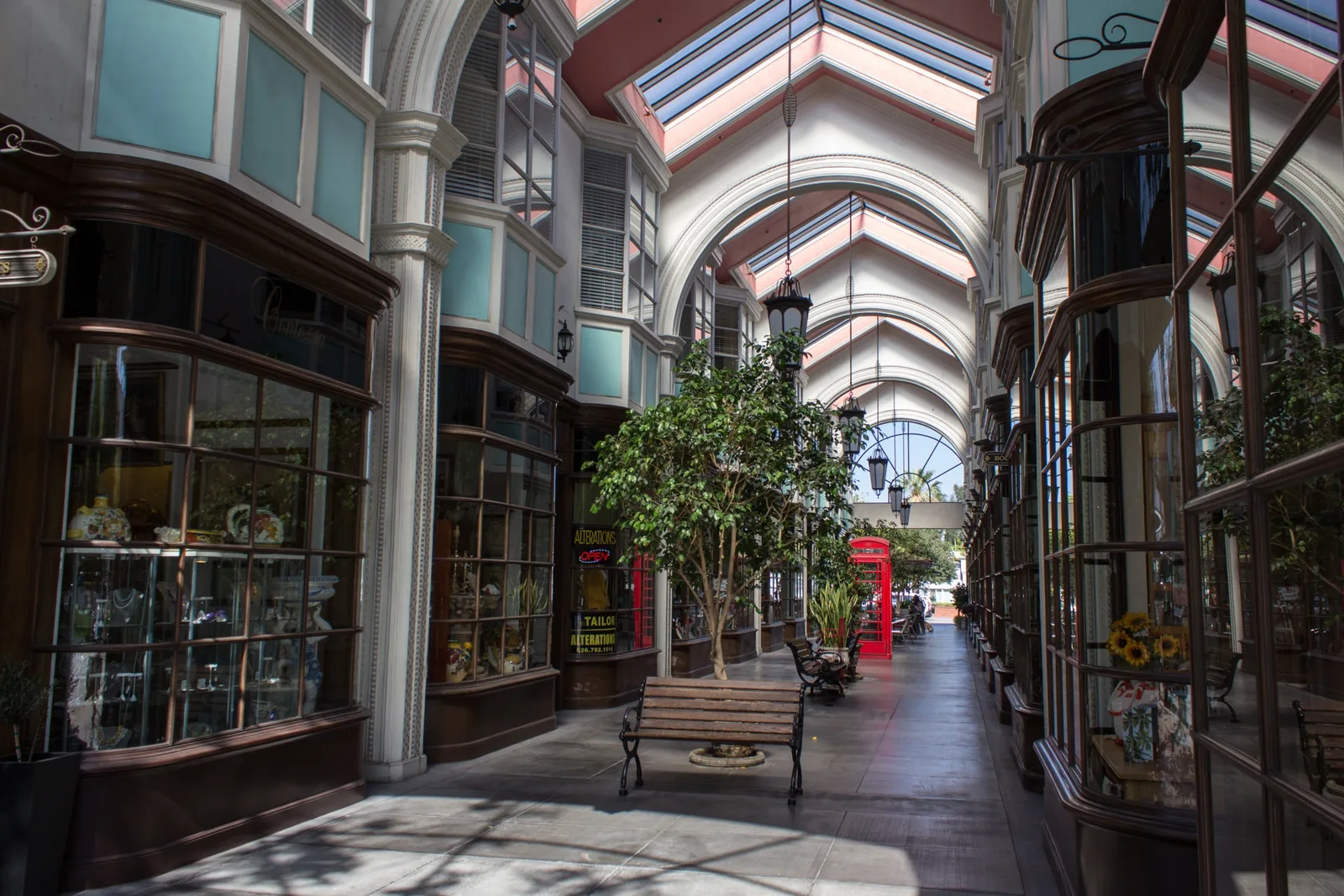 Covered shopping arcade with a vaulted glass roof, potted trees and bench