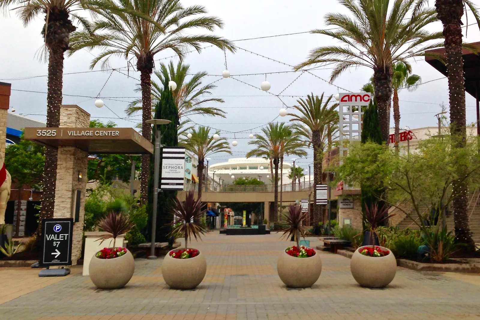 Palm lined outdoor plaza with round planters, string lights and an AMC cinema