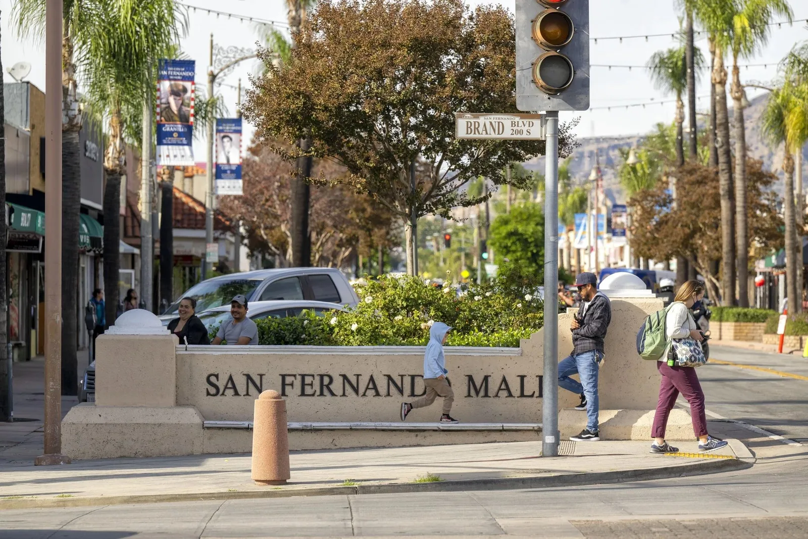 Stone SAN FERNANDO MALL sign beside a palm lined street with people crossing