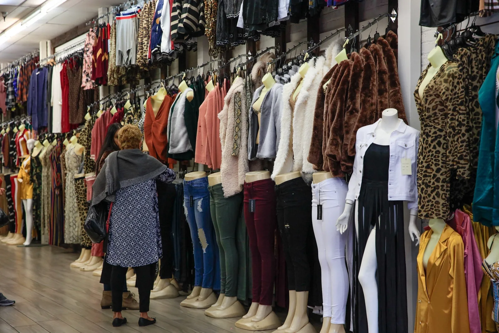 Sidewalk racks crammed with clothing and mannequins as a shopper browses