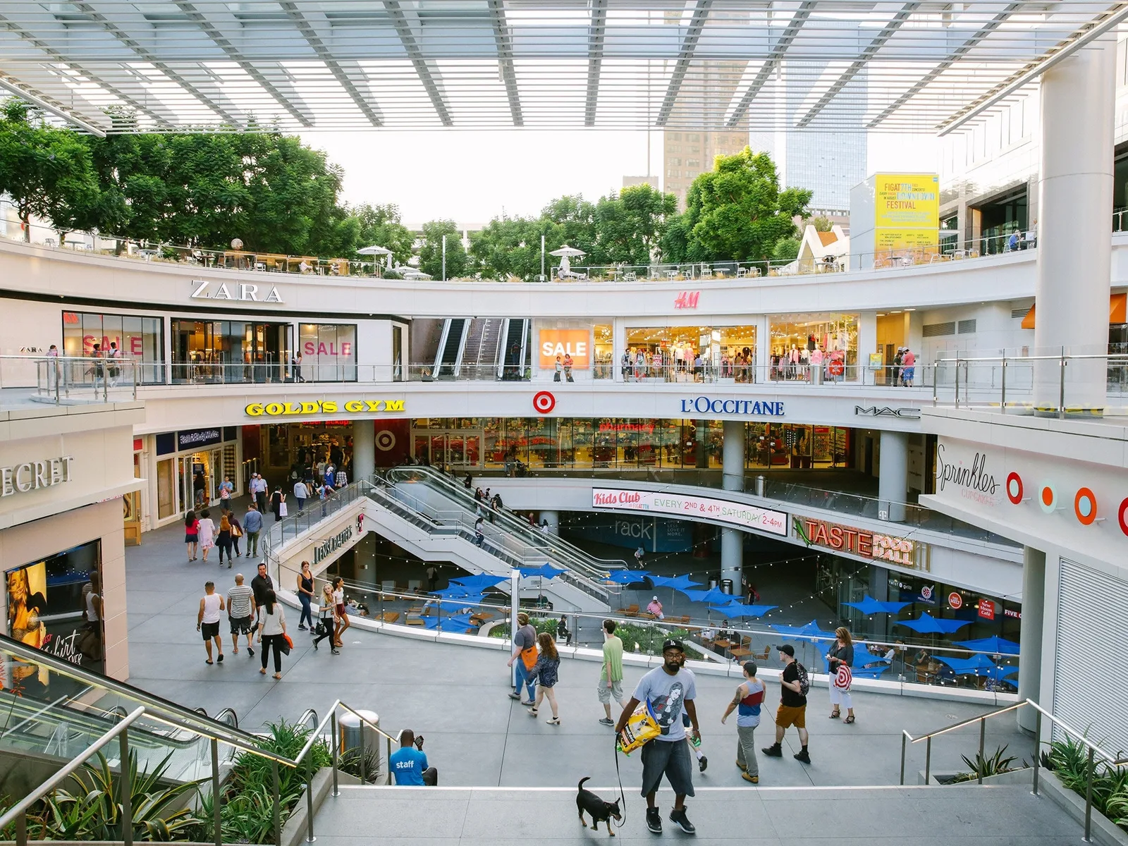 Multi level open air mall with escalators, chain store signs and shoppers below