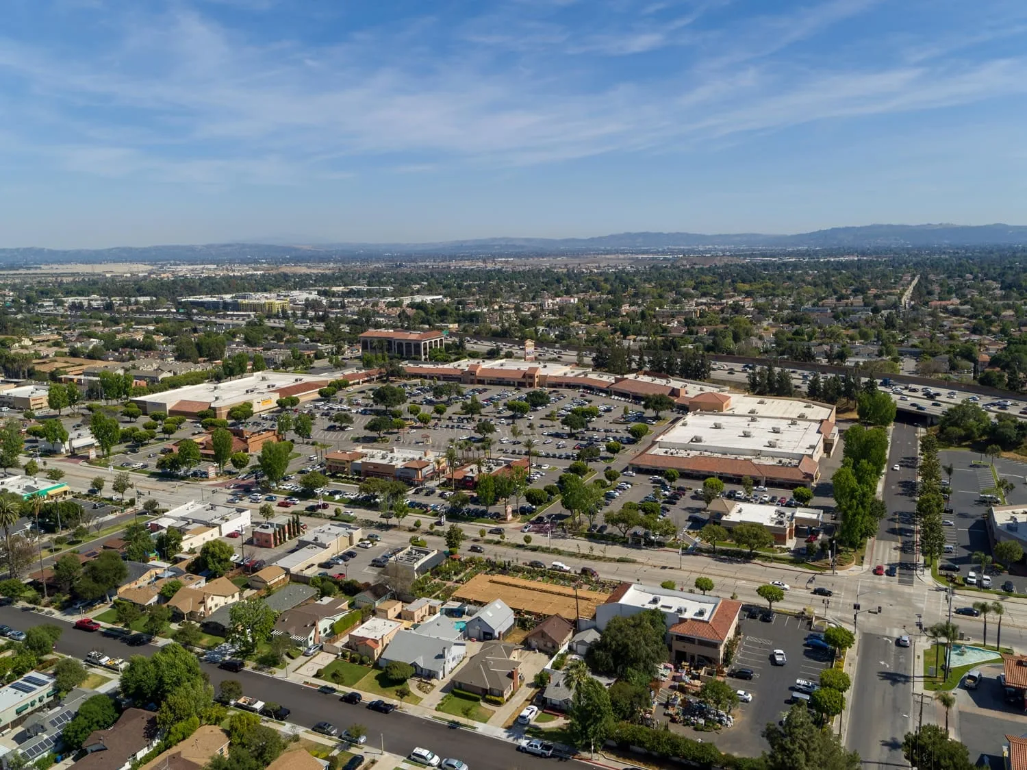 Aerial over a low rise shopping centre, parking lots and distant mountains