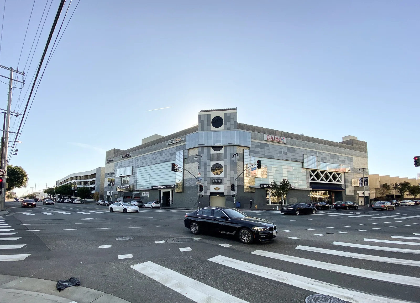 Wide intersection and crosswalk in front of a pale building with clock tower