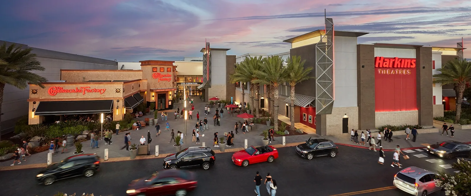 Cars and pedestrians outside a lit outdoor mall at dusk