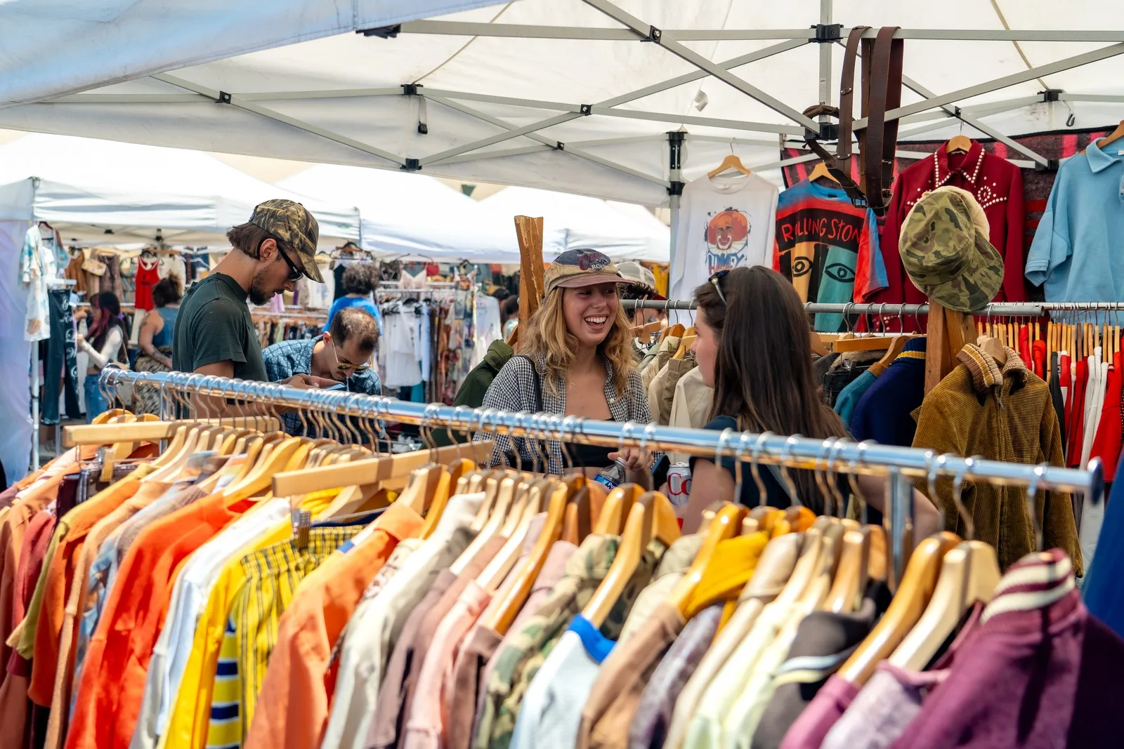 Colorful clothing racks under a white canopy as browsers shop an outdoor market