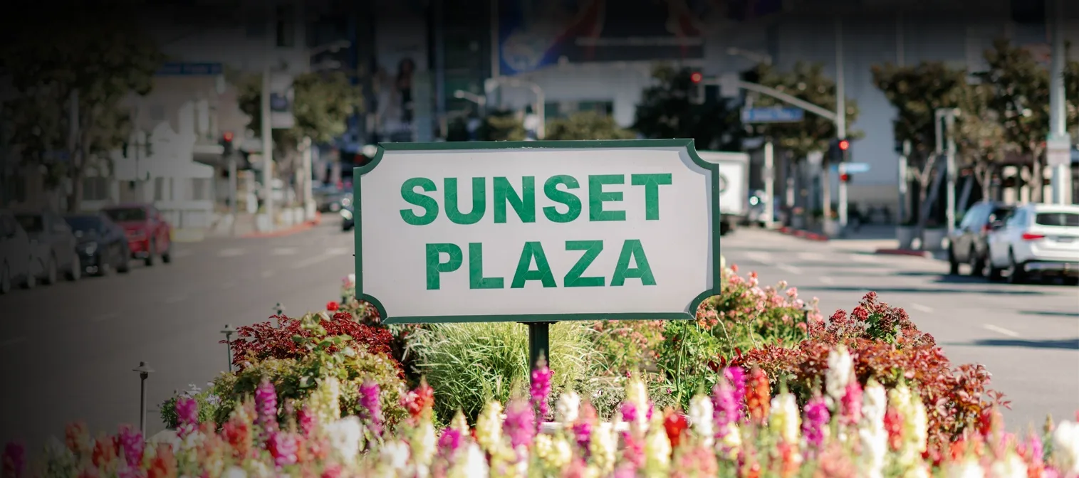 Green SUNSET PLAZA sign set in a bed of pink and white flowers