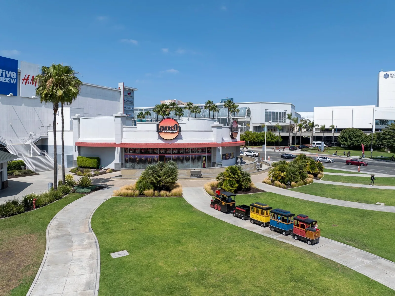 Outlet center behind a lawn with a small passenger train and palms