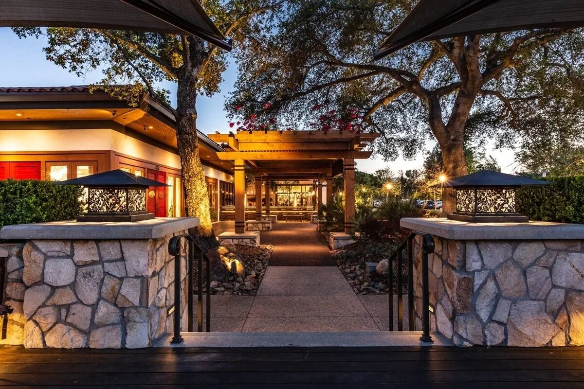 Stone pillars and oak trees framing a warmly lit entrance at twilight