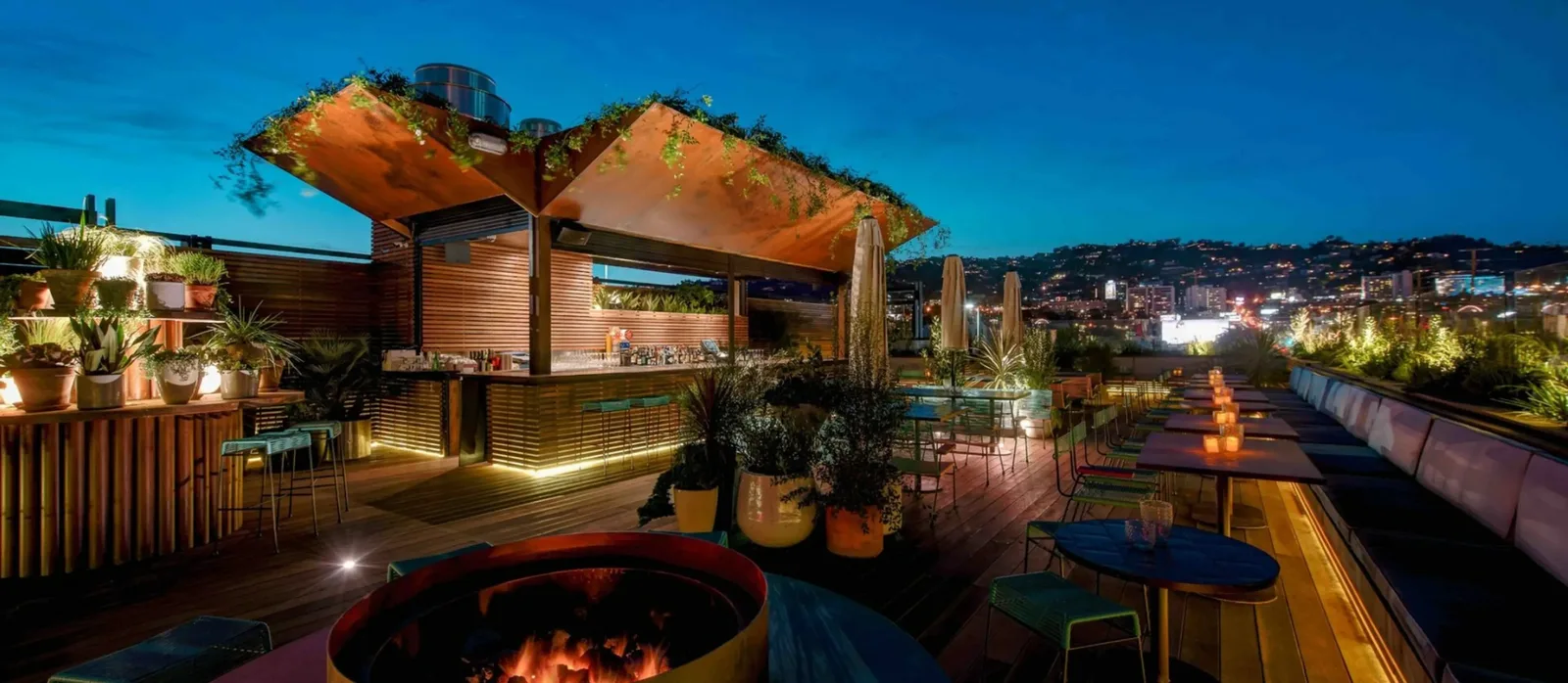 Rooftop bar at dusk with lit fire pit and planters