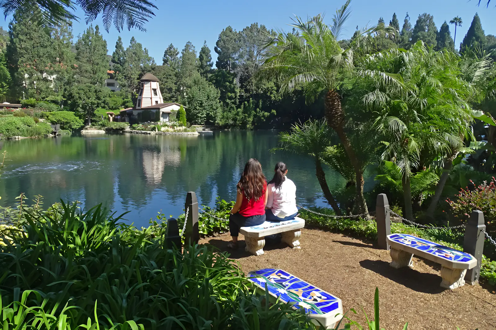 Visitors on a mosaic bench beside the spring-fed lake at the Self-Realization Fellowship Lake Shrine, with the windmill chapel across the water
